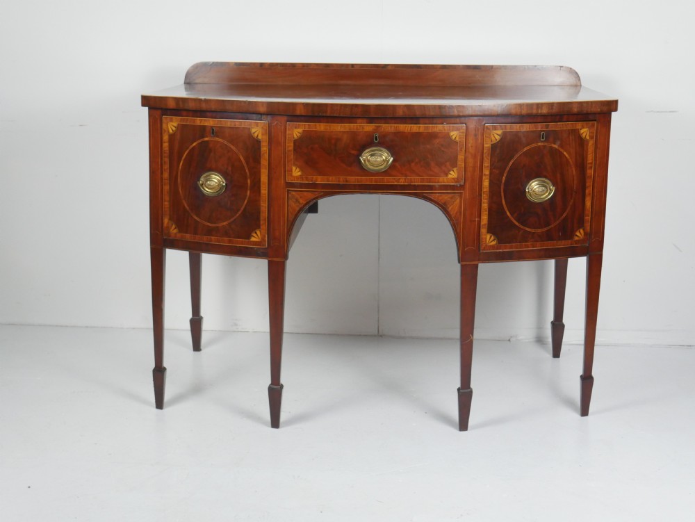 A Georgian bow-front mahogany sideboard featuring satinwood inlays, brass oval handles, and square tapered legs.