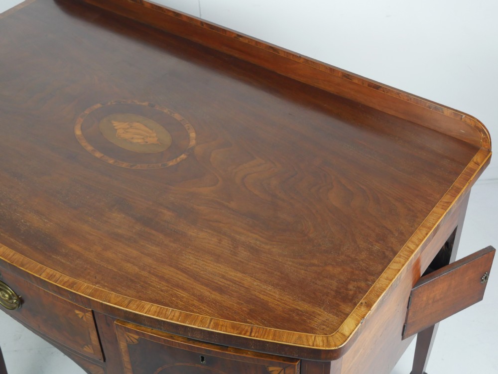 A Georgian bow-front mahogany sideboard featuring satinwood inlays, brass oval handles, and square tapered legs. View XIX