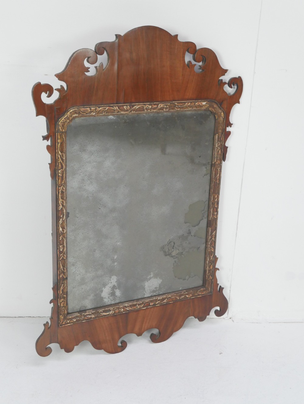 A Georgian mahogany wall mirror featuring a scroll-carved fretwork frame with an inner gilded slip border.