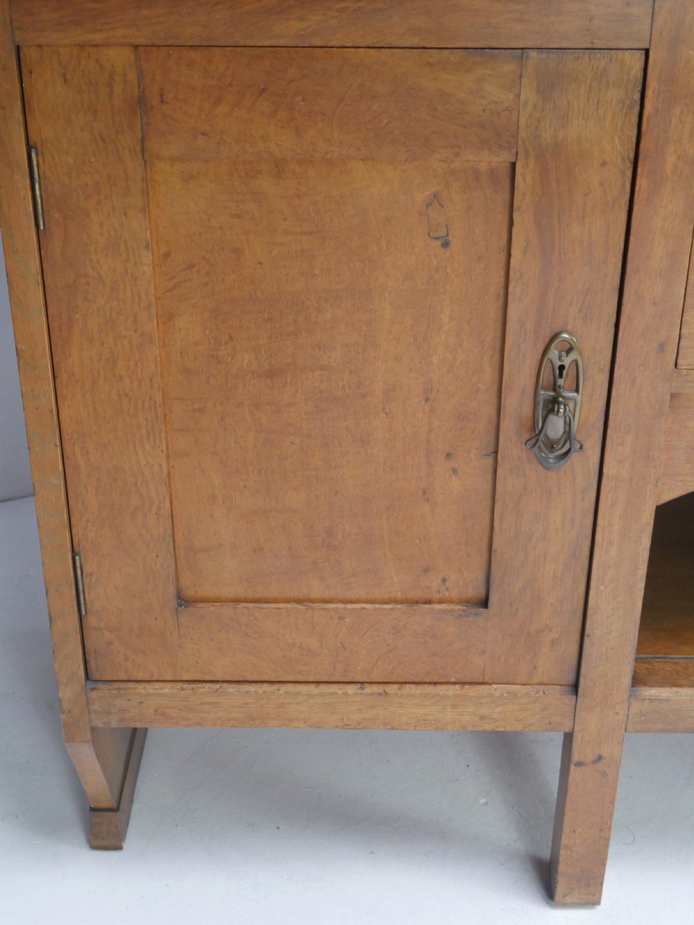 An Arts and Crafts solid oak dresser featuring an upper section with a central mirror flanked by two small cupboards, set above a lower sideboard base with drawers and side doors. View III