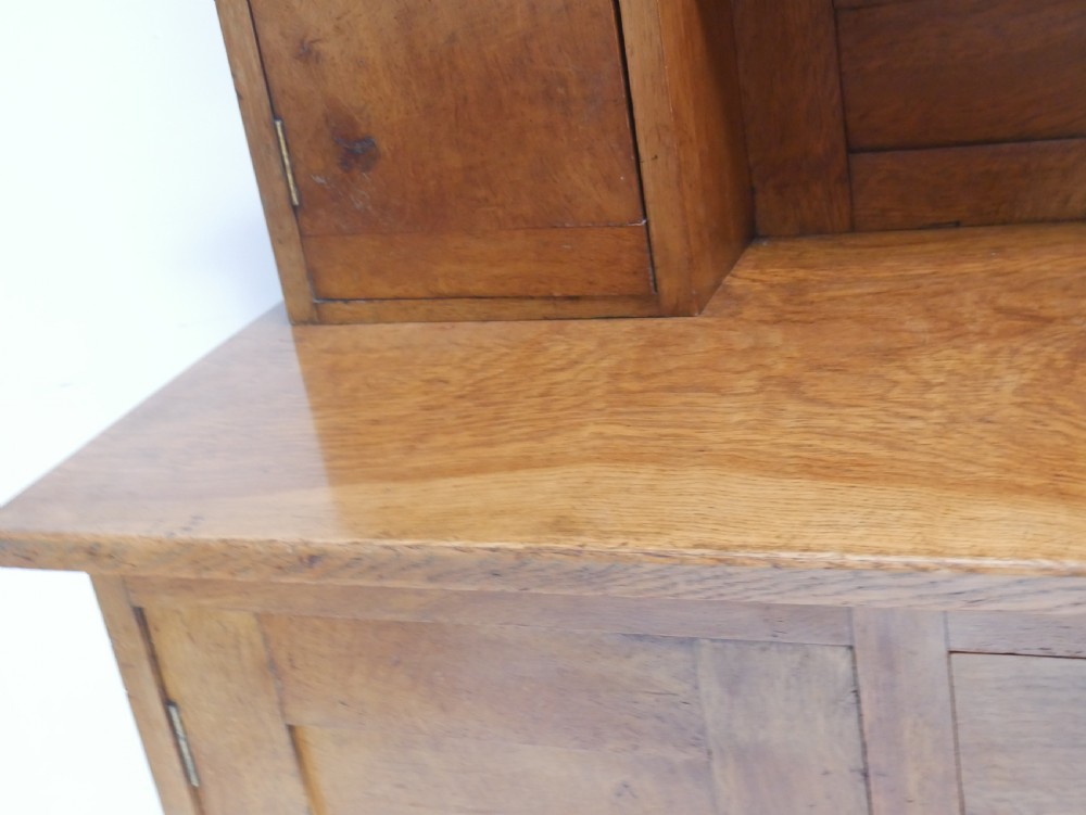 An Arts and Crafts solid oak dresser featuring an upper section with a central mirror flanked by two small cupboards, set above a lower sideboard base with drawers and side doors. View XVI