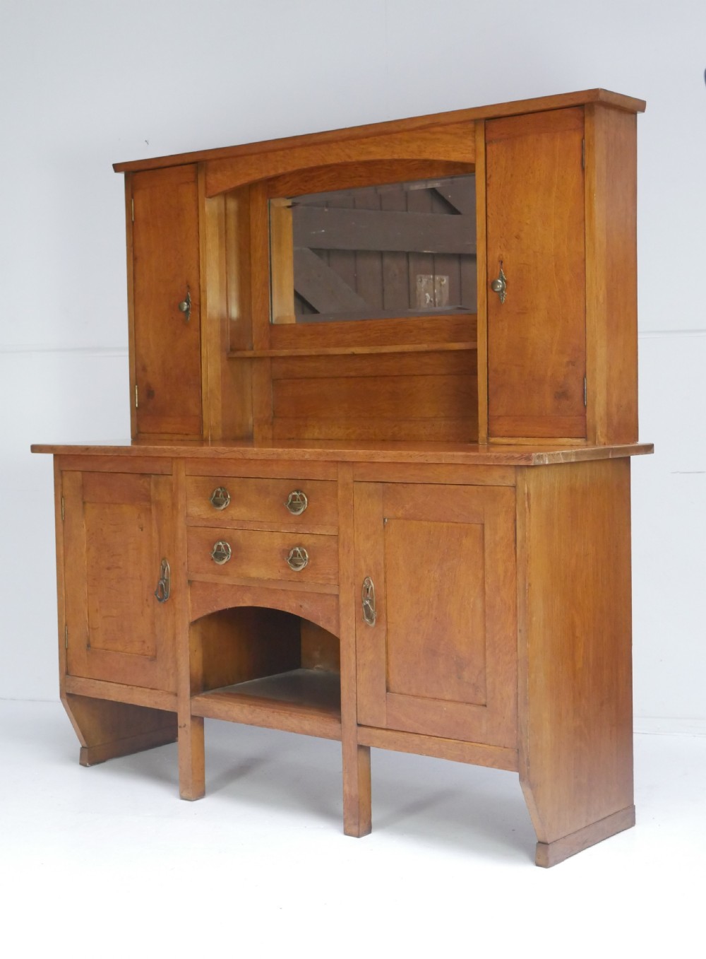 An Arts and Crafts solid oak dresser featuring an upper section with a central mirror flanked by two small cupboards, set above a lower sideboard base with drawers and side doors. View XIX