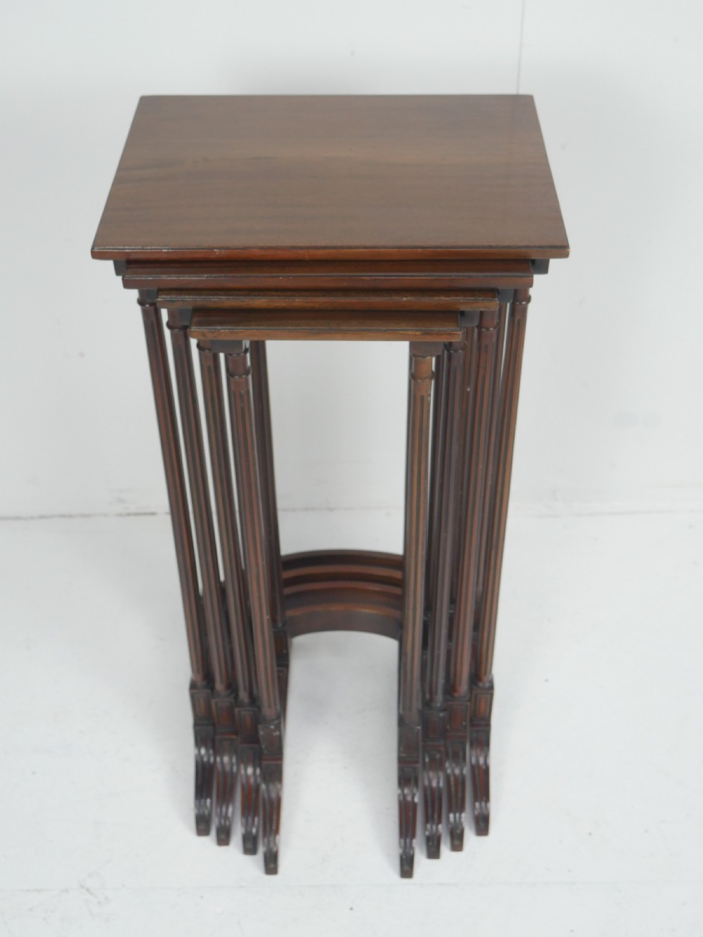 A set of four dark mahogany rectangular nesting tables with slender reeded legs and curved stretchers stacked together. View IX