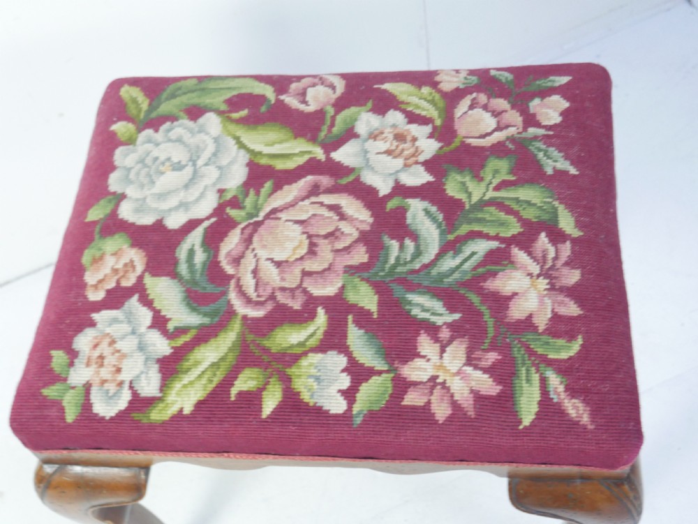 A 1920s low wooden footstool featuring carved cabriole legs and a rectangular seat upholstered in burgundy floral needlepoint tapestry. View II