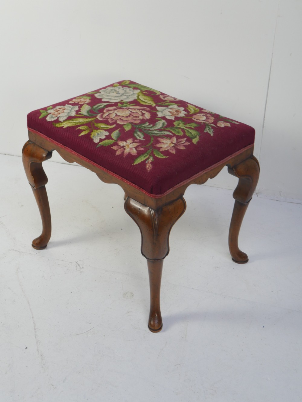 A 1920s low wooden footstool featuring carved cabriole legs and a rectangular seat upholstered in burgundy floral needlepoint tapestry. View III
