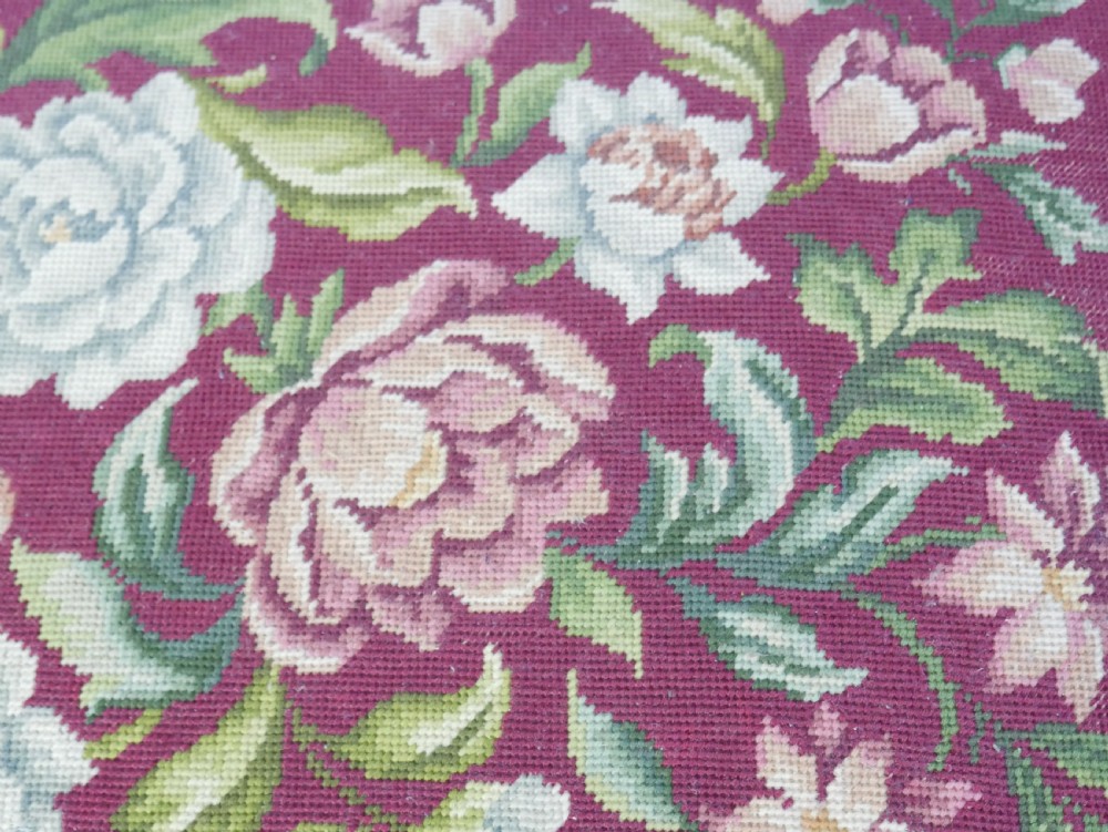 A 1920s low wooden footstool featuring carved cabriole legs and a rectangular seat upholstered in burgundy floral needlepoint tapestry. View V