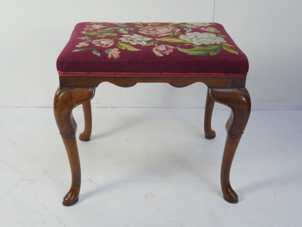 A 1920s low wooden footstool featuring carved cabriole legs and a rectangular seat upholstered in burgundy floral needlepoint tapestry. View VIII