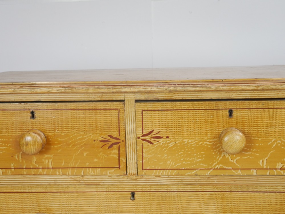 An antique Victorian painted pine chest featuring two short over two long drawers with faux graining, red line borders, wooden knobs, and turned feet. View II