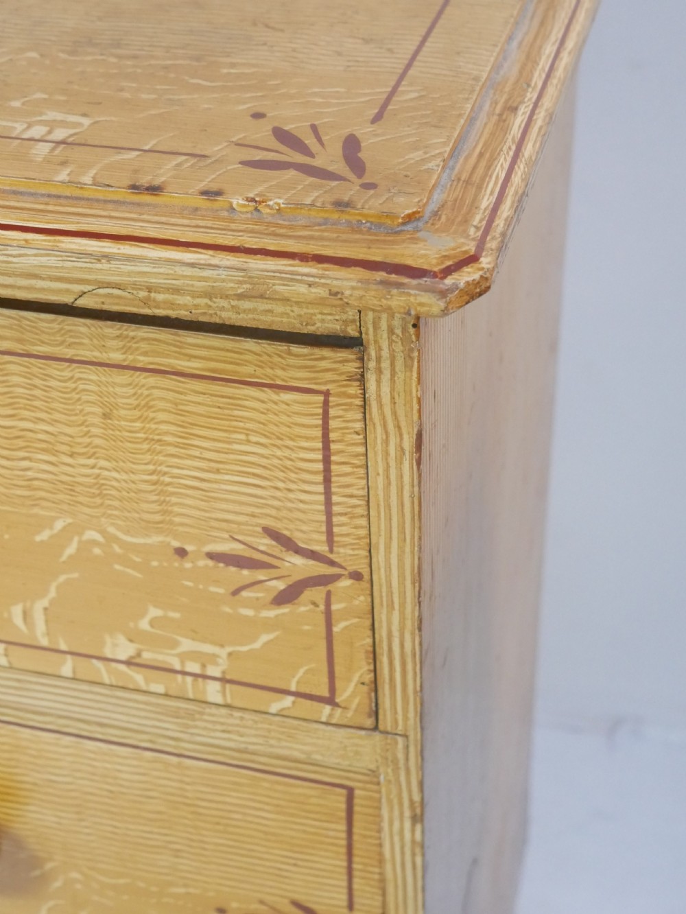 An antique Victorian painted pine chest featuring two short over two long drawers with faux graining, red line borders, wooden knobs, and turned feet. View III