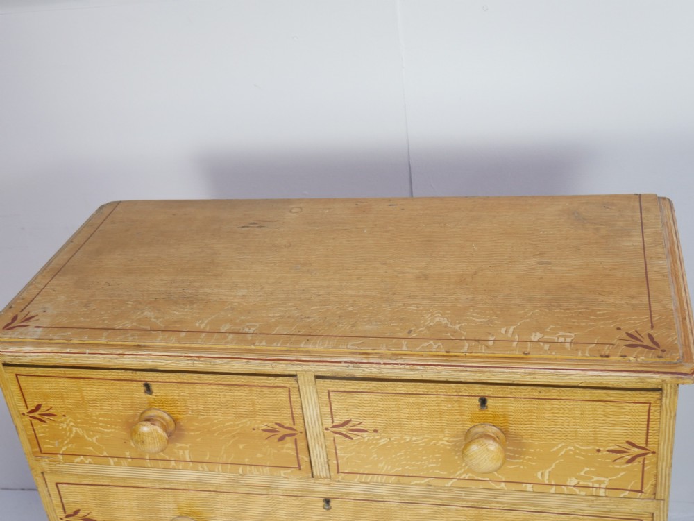 An antique Victorian painted pine chest featuring two short over two long drawers with faux graining, red line borders, wooden knobs, and turned feet. View V