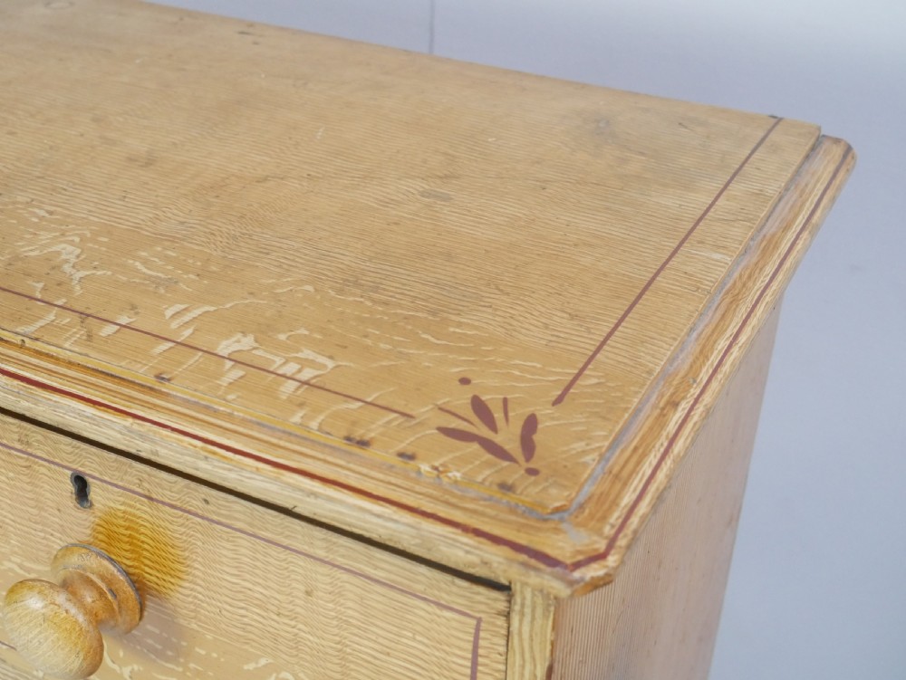An antique Victorian painted pine chest featuring two short over two long drawers with faux graining, red line borders, wooden knobs, and turned feet. View VI