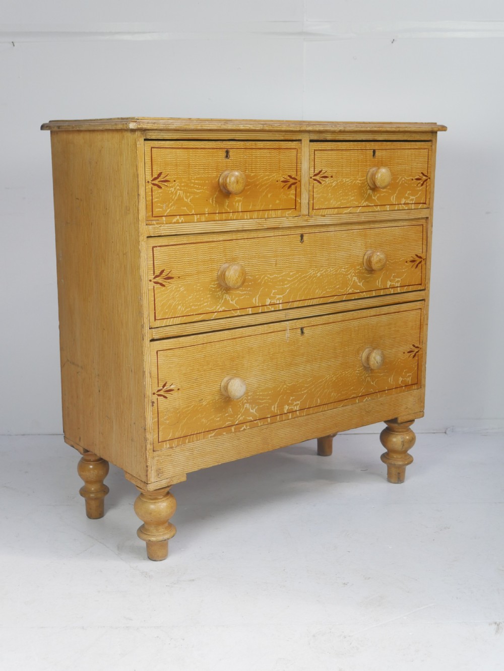 An antique Victorian painted pine chest featuring two short over two long drawers with faux graining, red line borders, wooden knobs, and turned feet. View XI