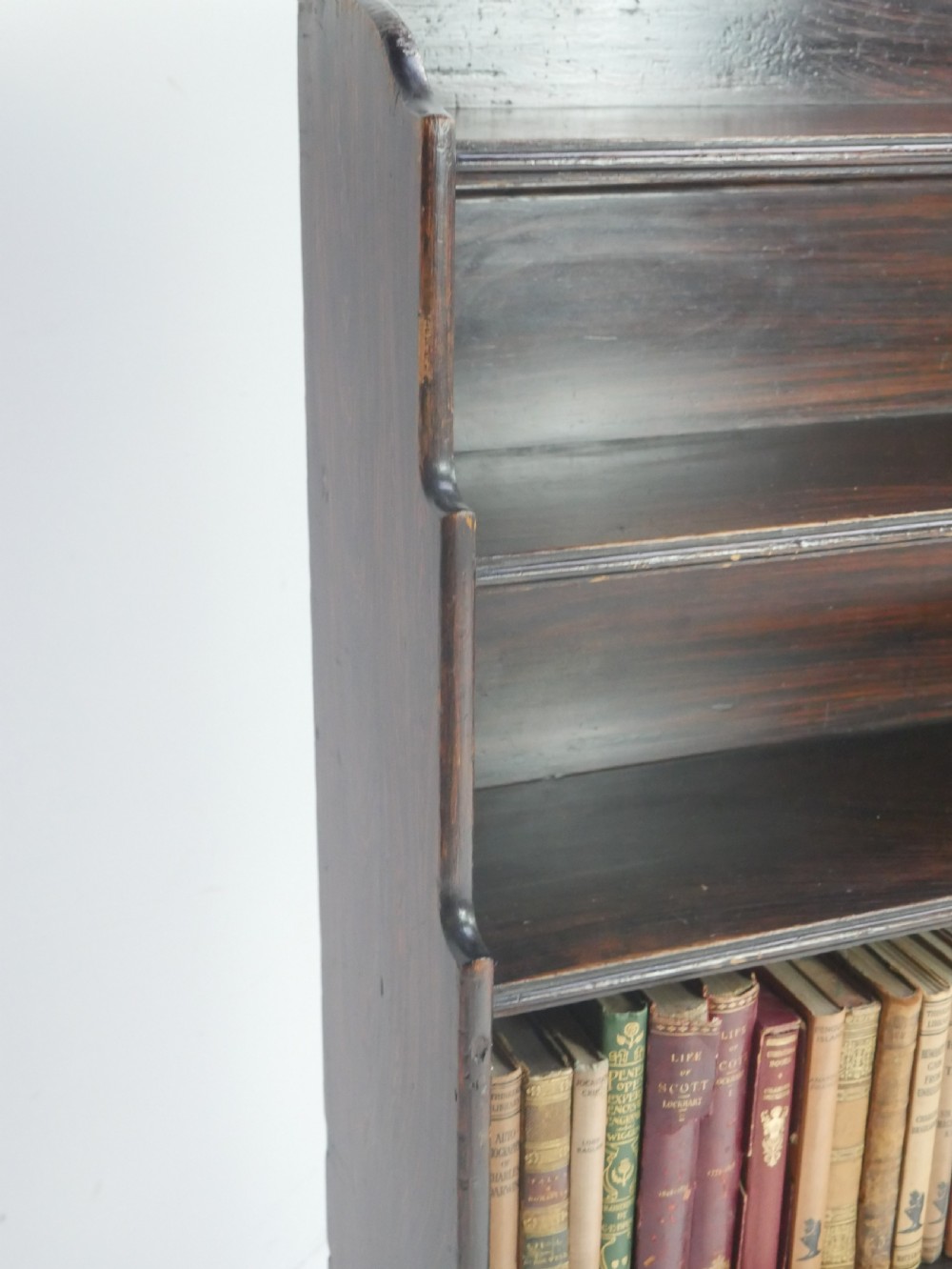 A dark brown 19th-century waterfall bookcase featuring four open stepped shelves, side profile cutouts, and turned legs. View V