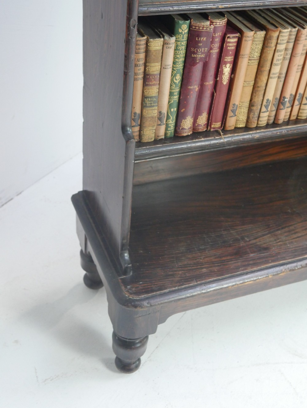A dark brown 19th-century waterfall bookcase featuring four open stepped shelves, side profile cutouts, and turned legs. View VI