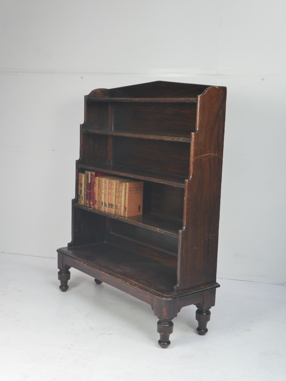 A dark brown 19th-century waterfall bookcase featuring four open stepped shelves, side profile cutouts, and turned legs. View XIV