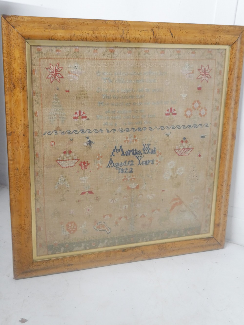 An 1822 hand-embroidered needlework sampler containing verse and decorative motifs, presented inside a glazed birdseye maple frame. View III