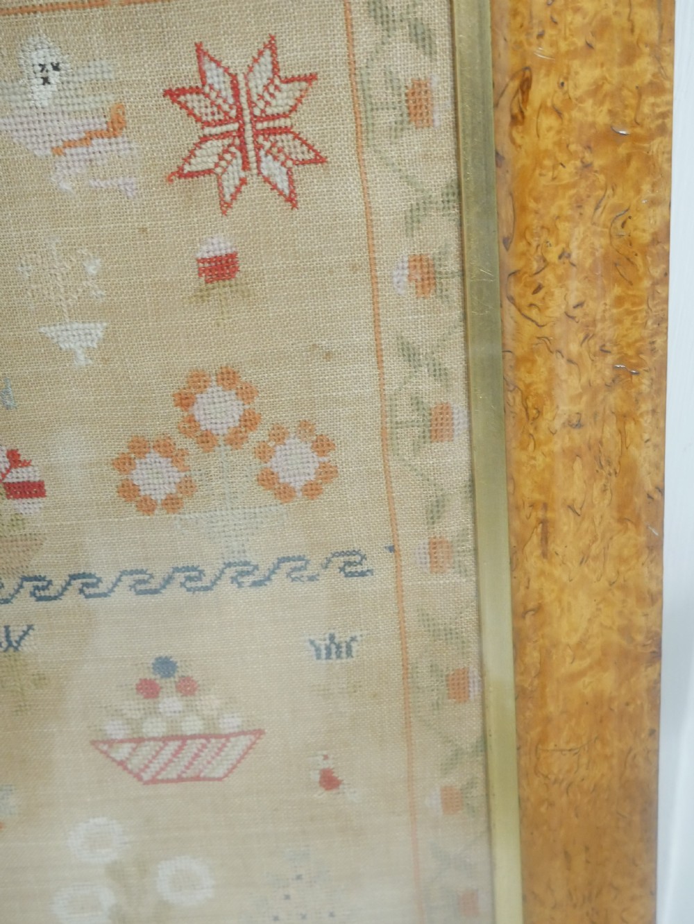 An 1822 hand-embroidered needlework sampler containing verse and decorative motifs, presented inside a glazed birdseye maple frame. View X