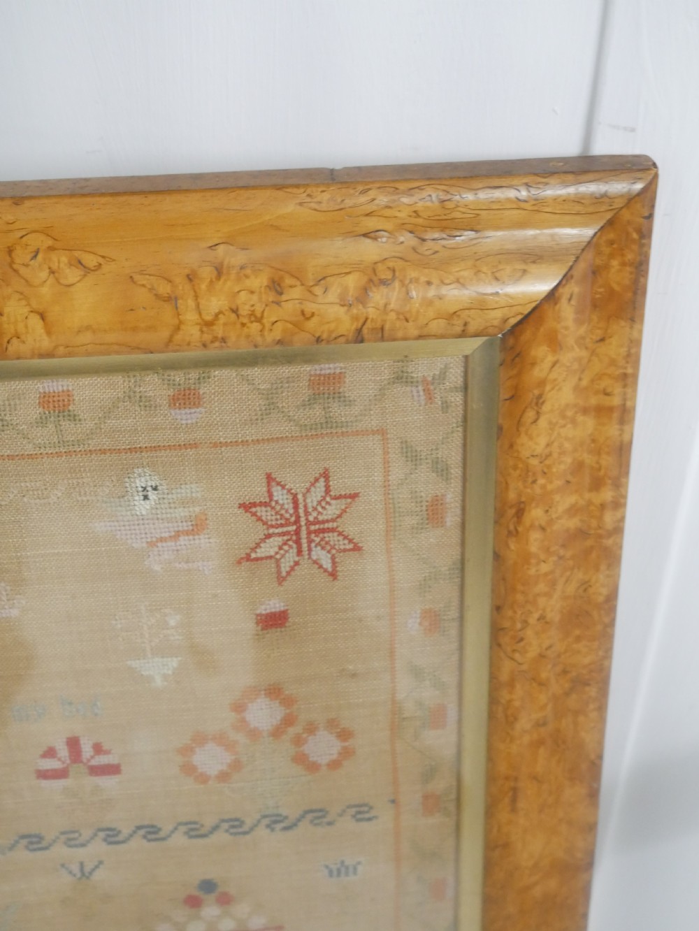 An 1822 hand-embroidered needlework sampler containing verse and decorative motifs, presented inside a glazed birdseye maple frame. View XI