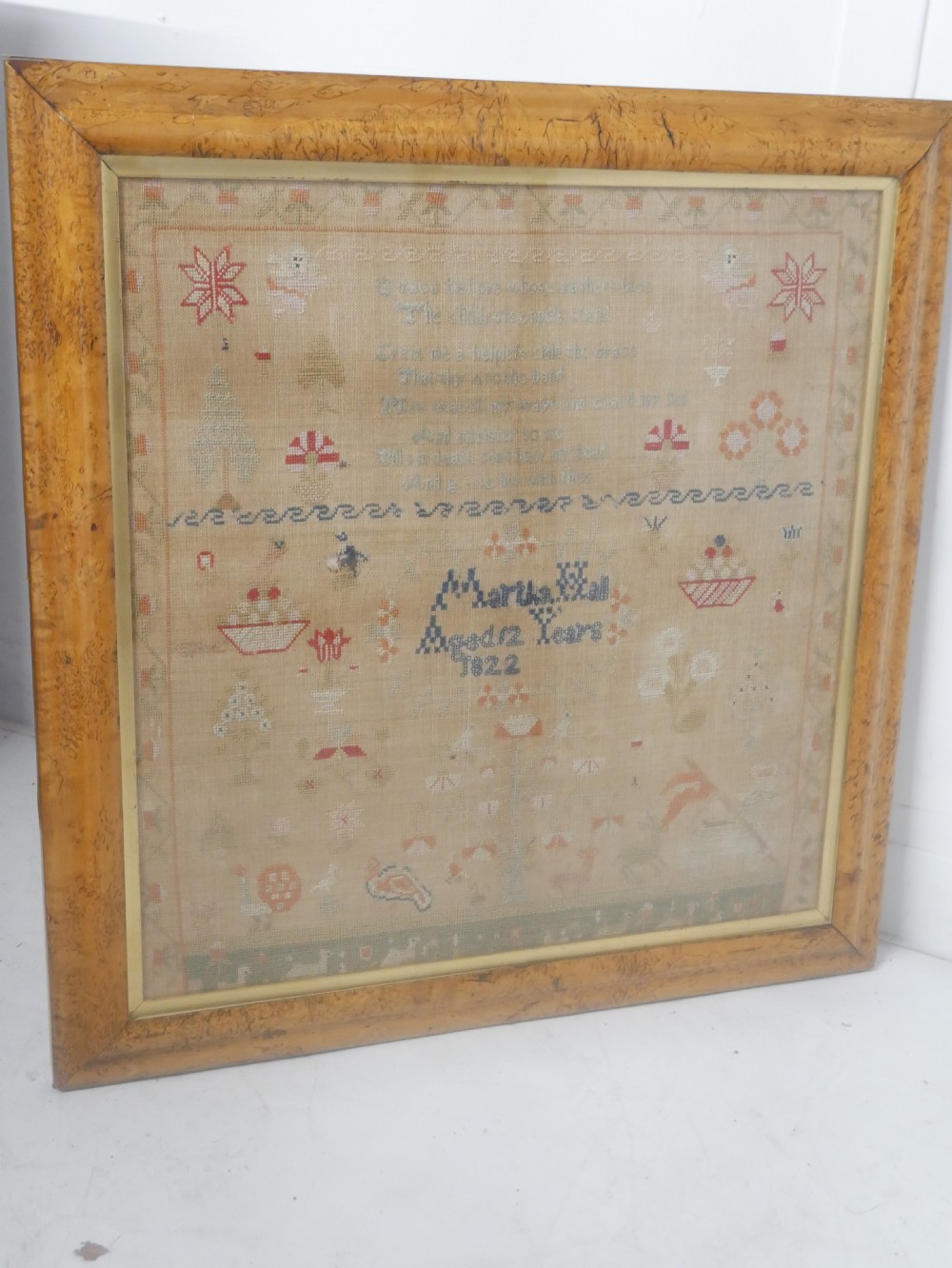 An 1822 hand-embroidered needlework sampler containing verse and decorative motifs, presented inside a glazed birdseye maple frame.