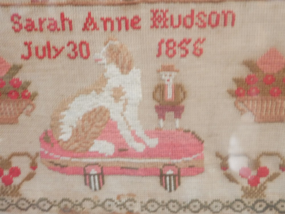 An 1856 Victorian needlework sampler featuring embroidered house, figure, bird, and floral motifs inside a golden maple wood frame. View II