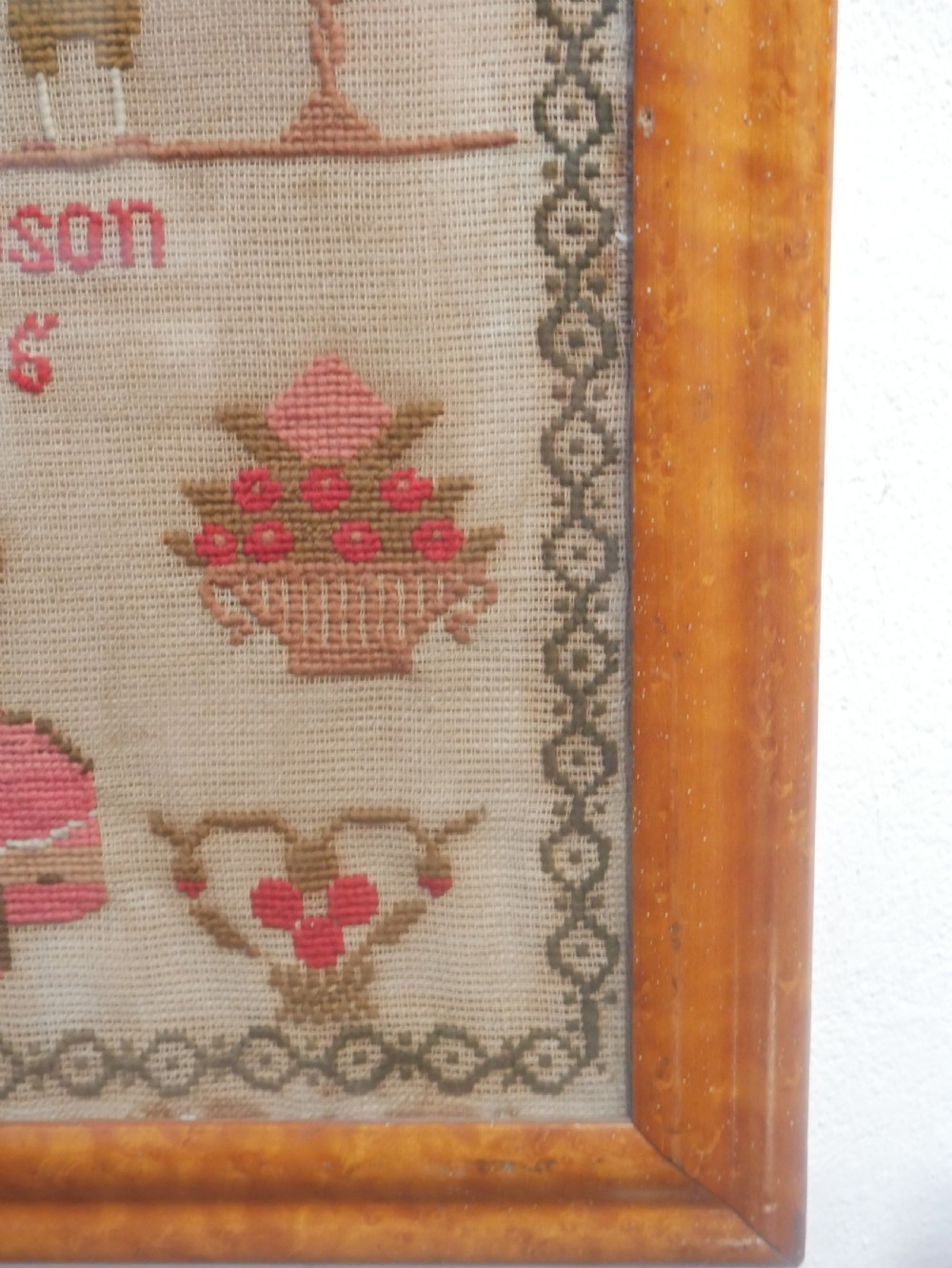 An 1856 Victorian needlework sampler featuring embroidered house, figure, bird, and floral motifs inside a golden maple wood frame. View III