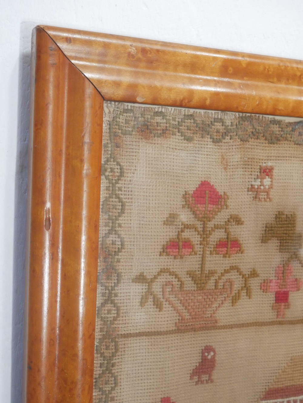 An 1856 Victorian needlework sampler featuring embroidered house, figure, bird, and floral motifs inside a golden maple wood frame. View VI