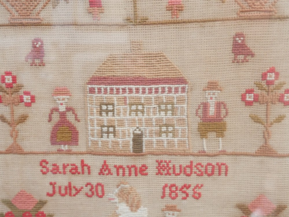 An 1856 Victorian needlework sampler featuring embroidered house, figure, bird, and floral motifs inside a golden maple wood frame. View VIII