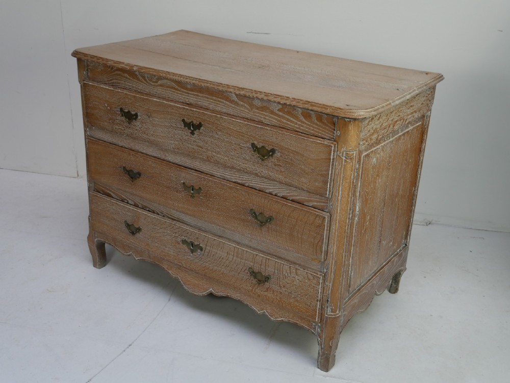An 18th-century French provincial limed oak chest of drawers featuring three full-width drawers with brass handles and a scalloped apron. View II