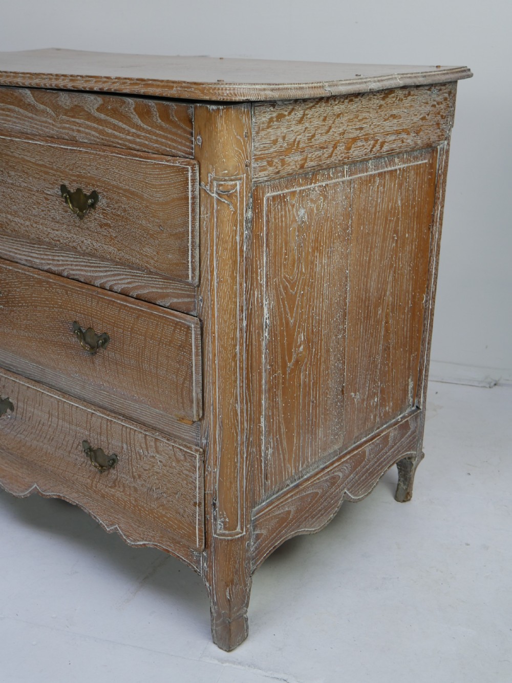 An 18th-century French provincial limed oak chest of drawers featuring three full-width drawers with brass handles and a scalloped apron. View III