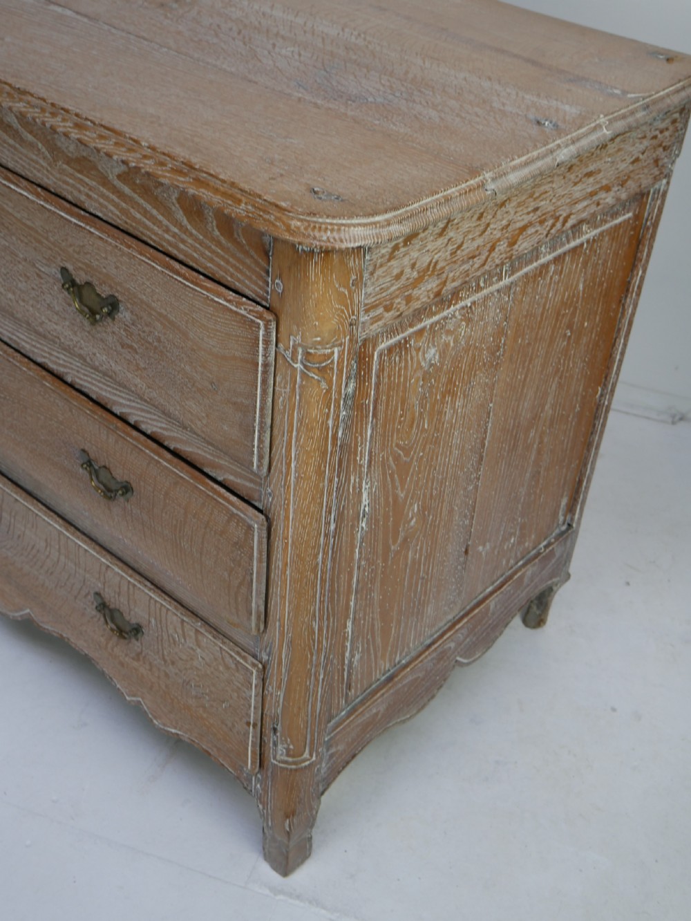 An 18th-century French provincial limed oak chest of drawers featuring three full-width drawers with brass handles and a scalloped apron. View VI