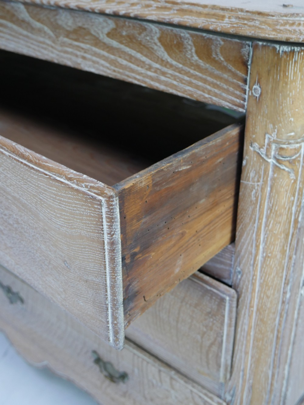 An 18th-century French provincial limed oak chest of drawers featuring three full-width drawers with brass handles and a scalloped apron. View VIII