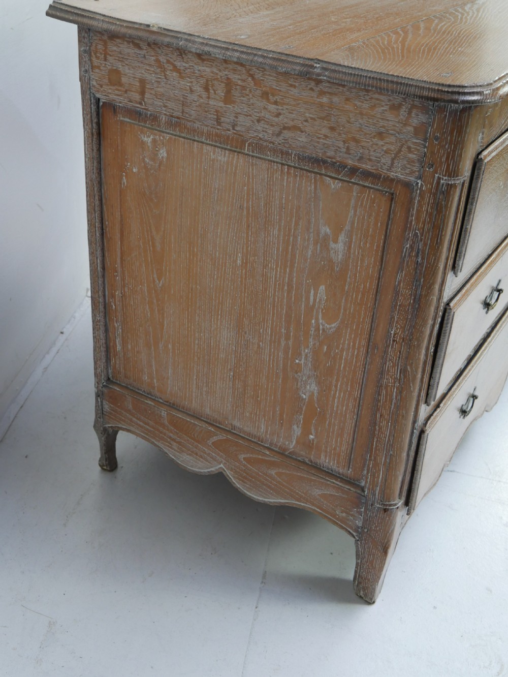 An 18th-century French provincial limed oak chest of drawers featuring three full-width drawers with brass handles and a scalloped apron. View IX