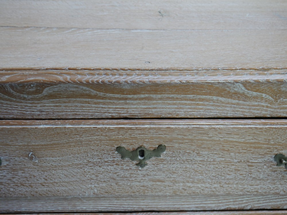 An 18th-century French provincial limed oak chest of drawers featuring three full-width drawers with brass handles and a scalloped apron. View X