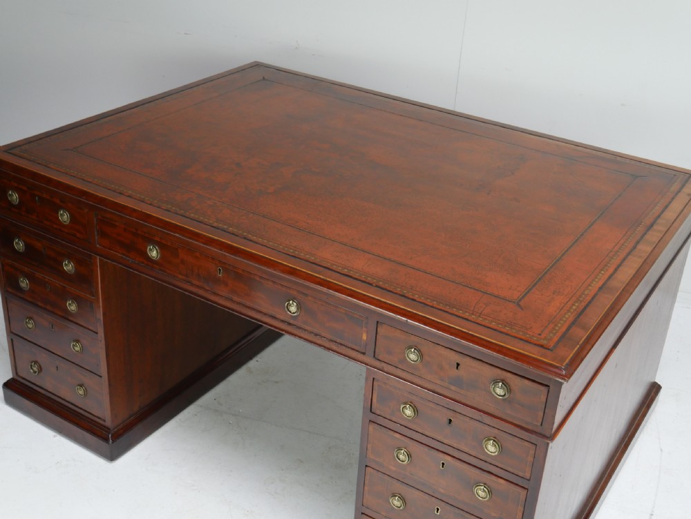 A 19th-century mahogany kneehole partners desk featuring twin pedestals, multiple drawers with brass drop handles, and a flat rectangular writing top. View X