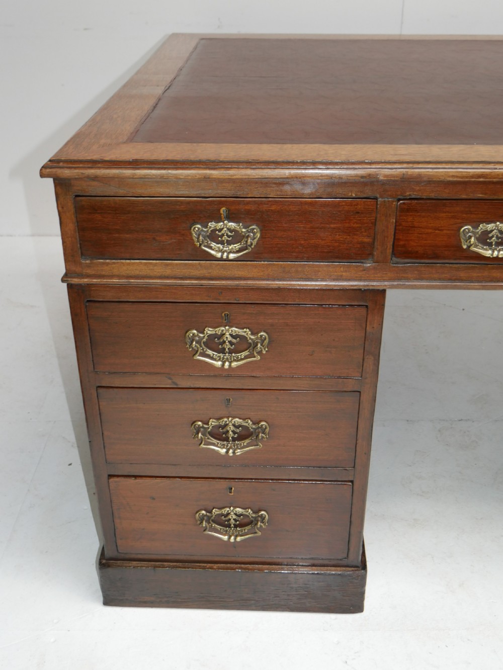 An antique oak partners kneehole desk featuring a leather-inset writing top, brass handles, and twin drawer pedestals on a plinth base. View II