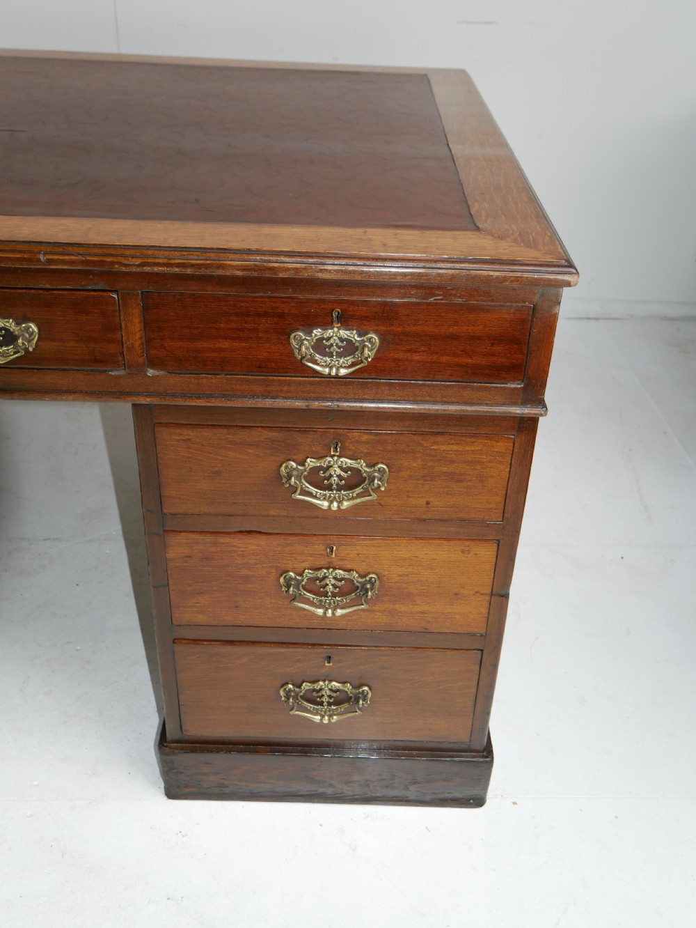 An antique oak partners kneehole desk featuring a leather-inset writing top, brass handles, and twin drawer pedestals on a plinth base. View III