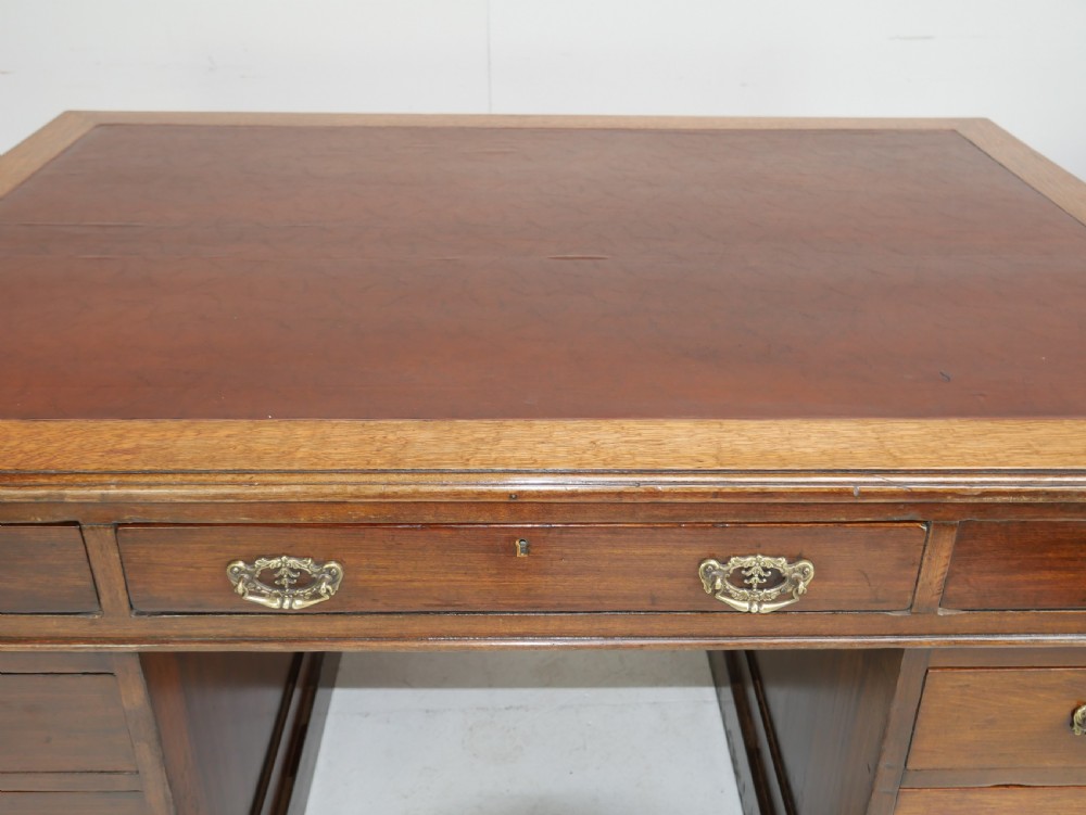 An antique oak partners kneehole desk featuring a leather-inset writing top, brass handles, and twin drawer pedestals on a plinth base. View V