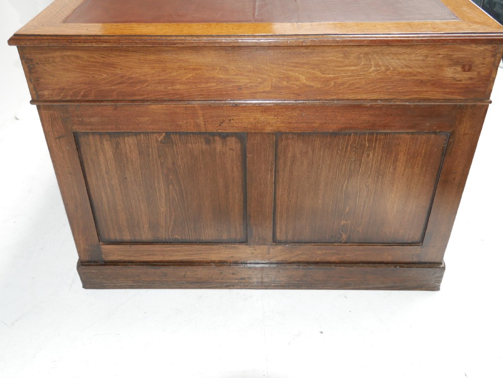 An antique oak partners kneehole desk featuring a leather-inset writing top, brass handles, and twin drawer pedestals on a plinth base. View VI
