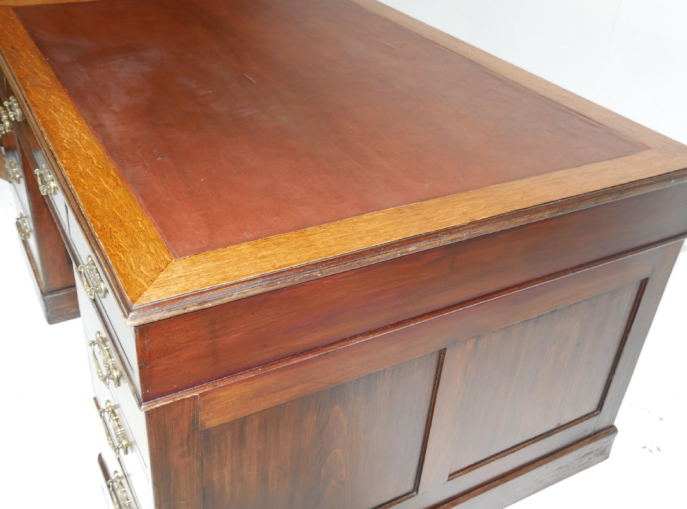 An antique oak partners kneehole desk featuring a leather-inset writing top, brass handles, and twin drawer pedestals on a plinth base. View VII