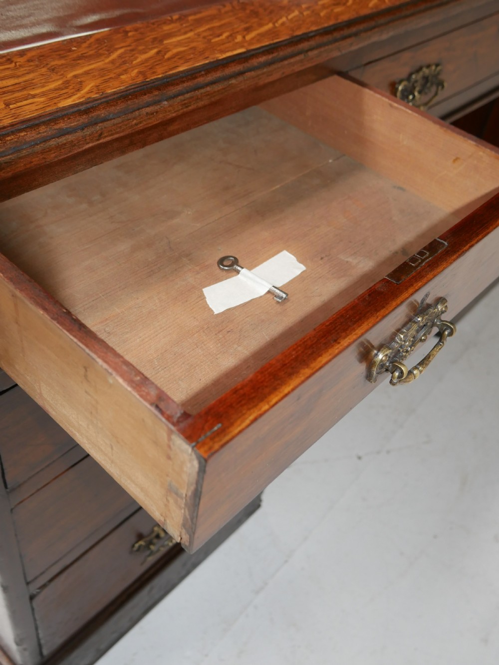An antique oak partners kneehole desk featuring a leather-inset writing top, brass handles, and twin drawer pedestals on a plinth base. View X