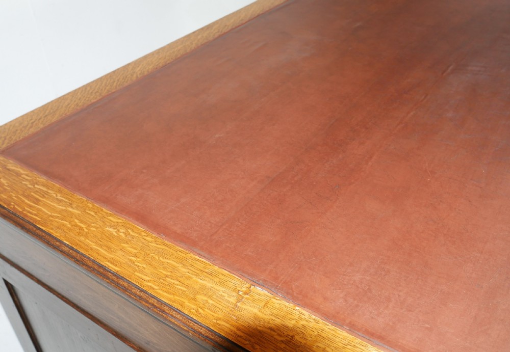 An antique oak partners kneehole desk featuring a leather-inset writing top, brass handles, and twin drawer pedestals on a plinth base. View XI