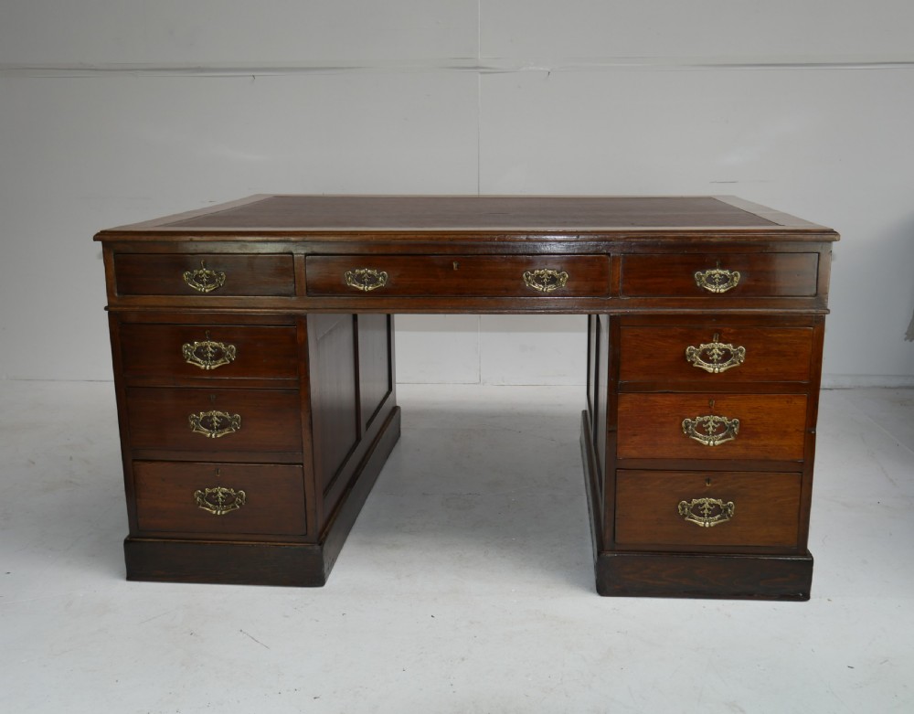 An antique oak partners kneehole desk featuring a leather-inset writing top, brass handles, and twin drawer pedestals on a plinth base. View XII