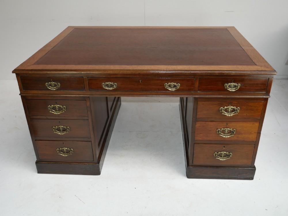 An antique oak partners kneehole desk featuring a leather-inset writing top, brass handles, and twin drawer pedestals on a plinth base. View XIII