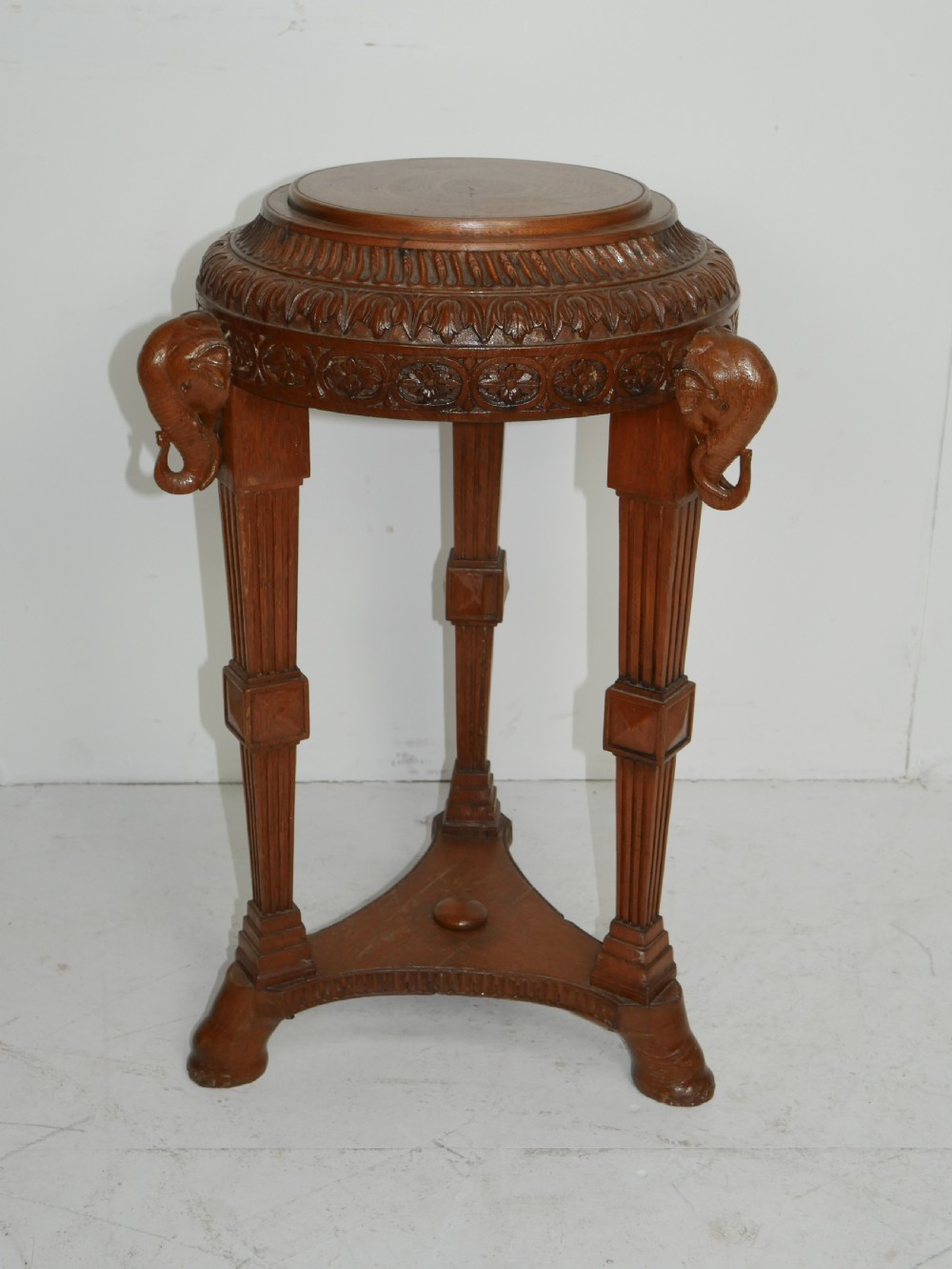 A circular Anglo-Indian carved hardwood plant stand supported by three fluted legs topped with carved elephant heads.