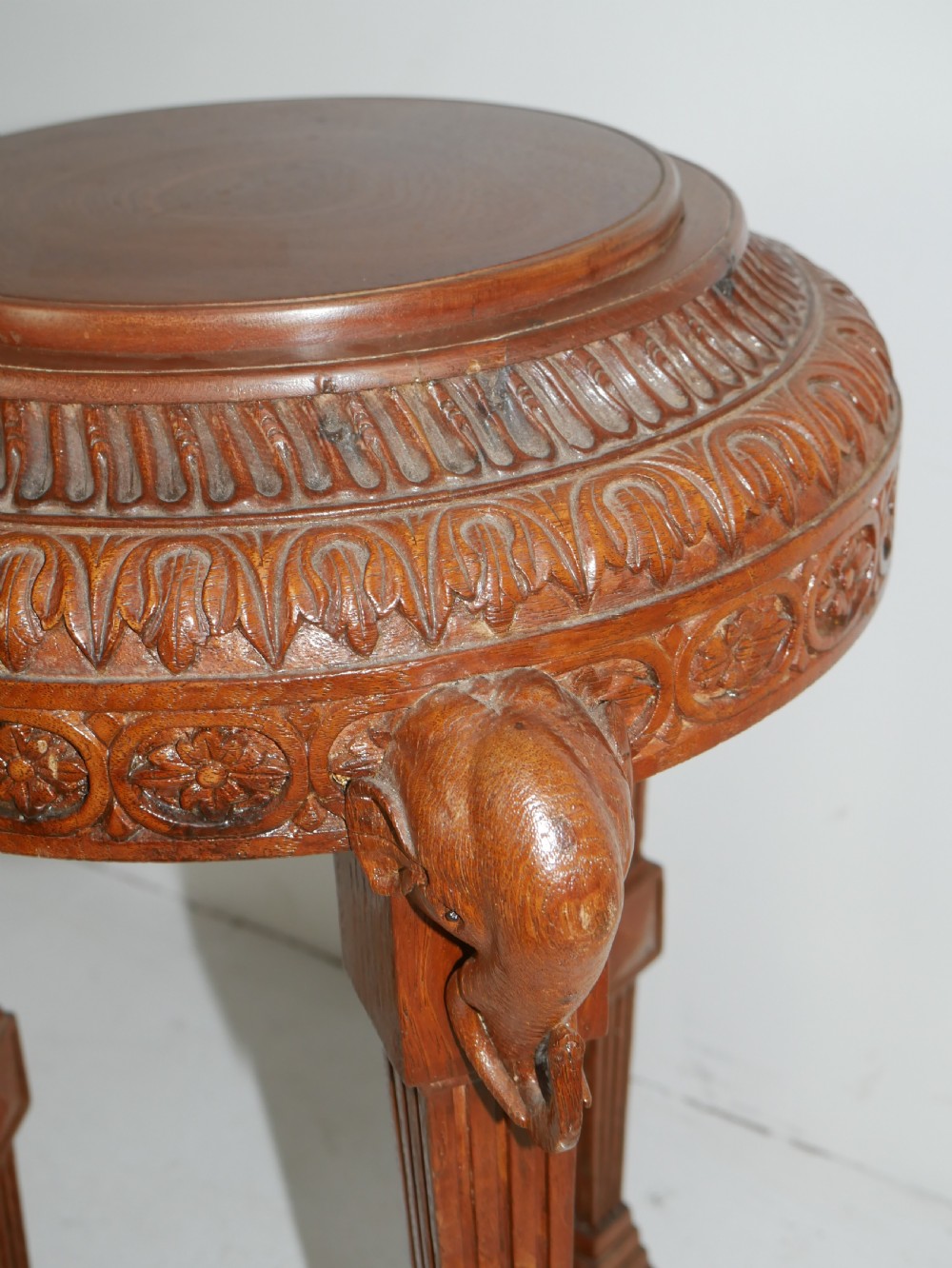 A circular Anglo-Indian carved hardwood plant stand supported by three fluted legs topped with carved elephant heads. View V