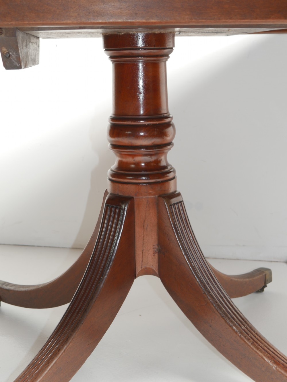 A Georgian mahogany centre table featuring a rounded rectangular top supported by a central pedestal with four reeded splayed legs and brass castors. View V