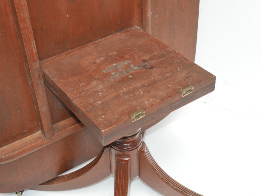 A Georgian mahogany centre table featuring a rounded rectangular top supported by a central pedestal with four reeded splayed legs and brass castors. View IV