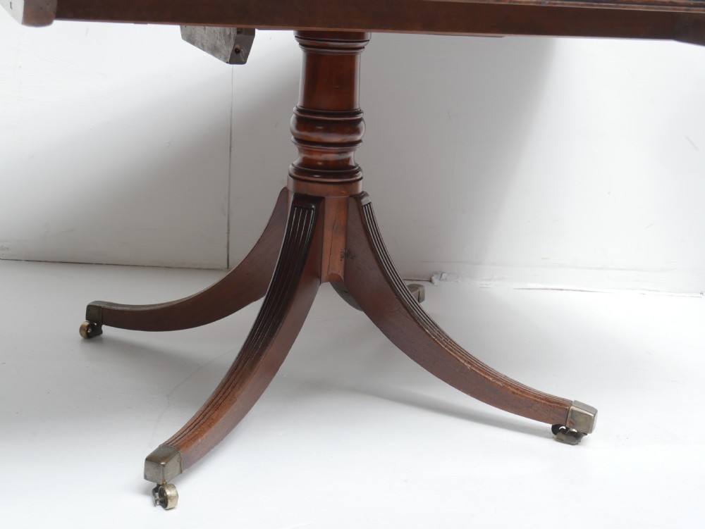 A Georgian mahogany centre table featuring a rounded rectangular top supported by a central pedestal with four reeded splayed legs and brass castors. View IX