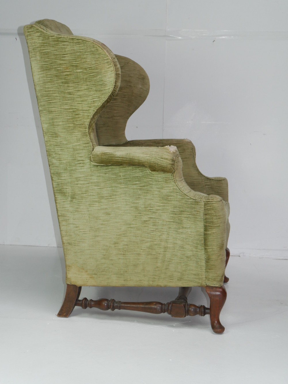 A high-backed wing armchair upholstered in textured olive green velvet with carved cabriole front legs and turned stretchers. View III