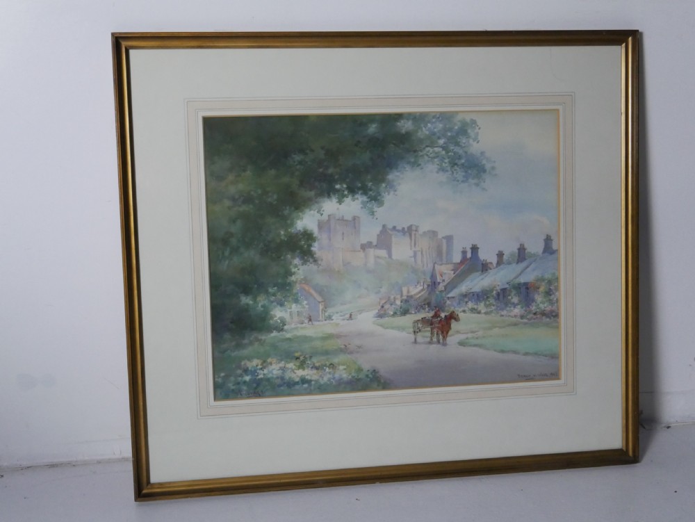A framed watercolour painting depicting a village street with a horse and cart leading towards Bamburgh Castle under a soft sky. View IV
